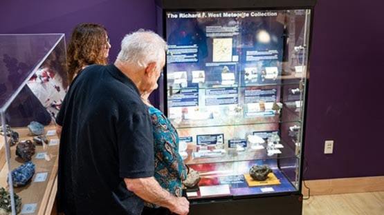 Visitors viewing meteorite specimens and an exhibit display case in a museum.