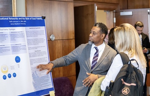 A researcher presenting a poster on organizational networks and goal fidelity to an audience member at an academic conference.