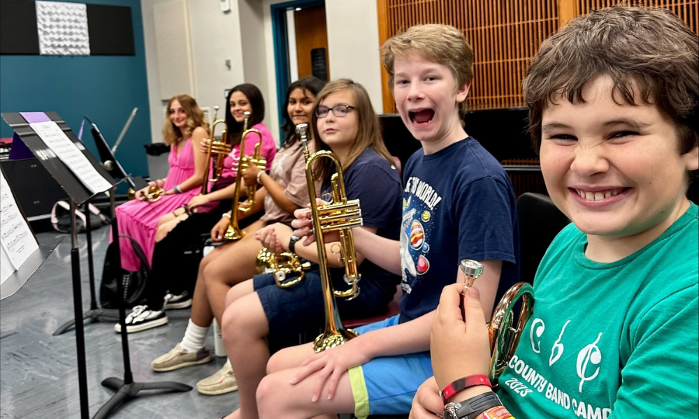 Middle school students smiling and making silly faces while holding trumpets