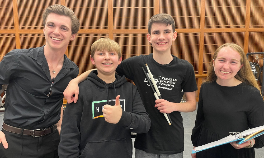 Students smiling and holding drumsticks and giving a thumbs up