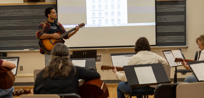 Man with guitar standing in front of guitar class