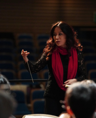 Woman talking to an orchestra with conducting baton in hand