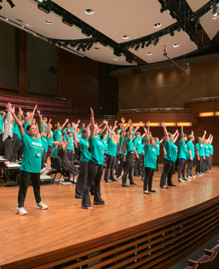Students on concert hall stage with arms in the air