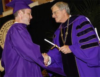 Photo of JMU President Linwood Rose handing a graduate his degree.