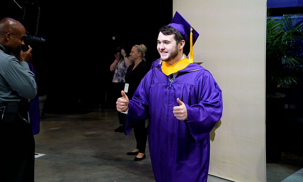 Tim Thome (’22) gives the thumbs up after walking across the Spring 2023 commencement stage at JMU's graduation celebration for the College of Health and Behavioral Sciences
