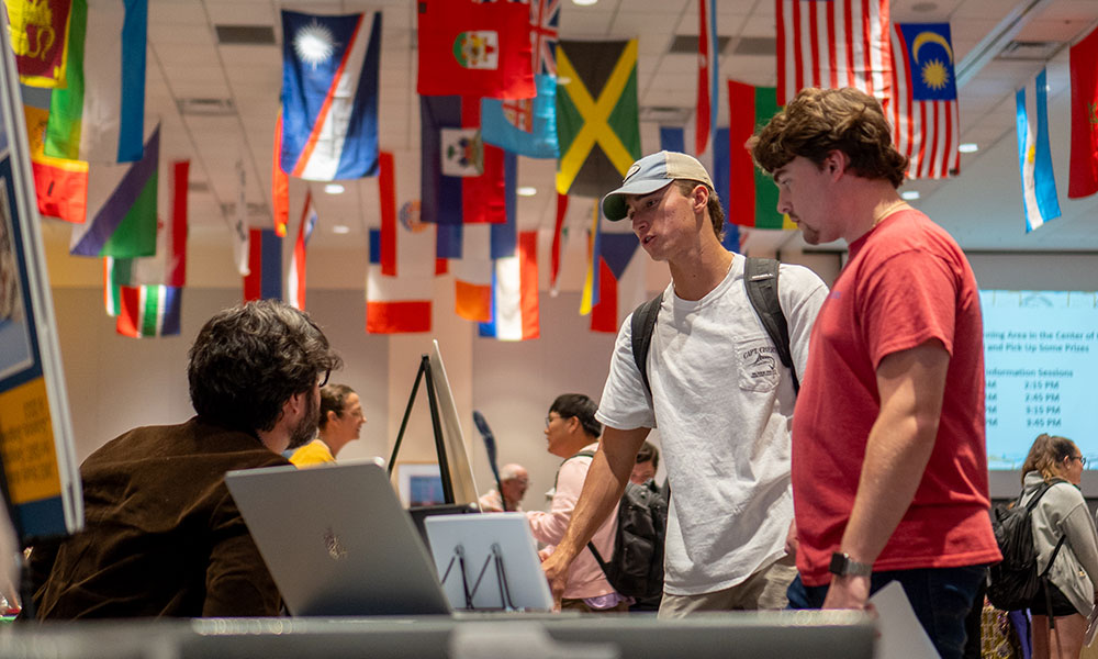 Male students converse with a person at a table.