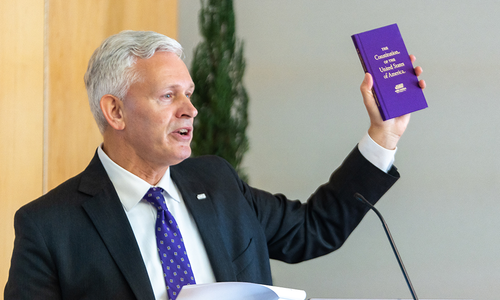 President Alger holds up a purple Constitution book.