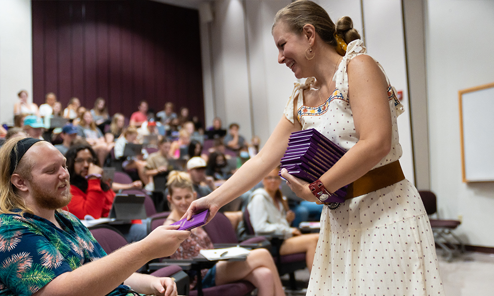 A woman hands out pocket Constitution books to students.