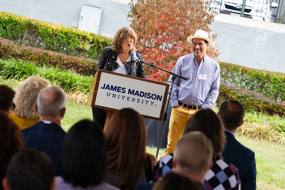 Linda Yates speaking at the podium next to Paul Holland