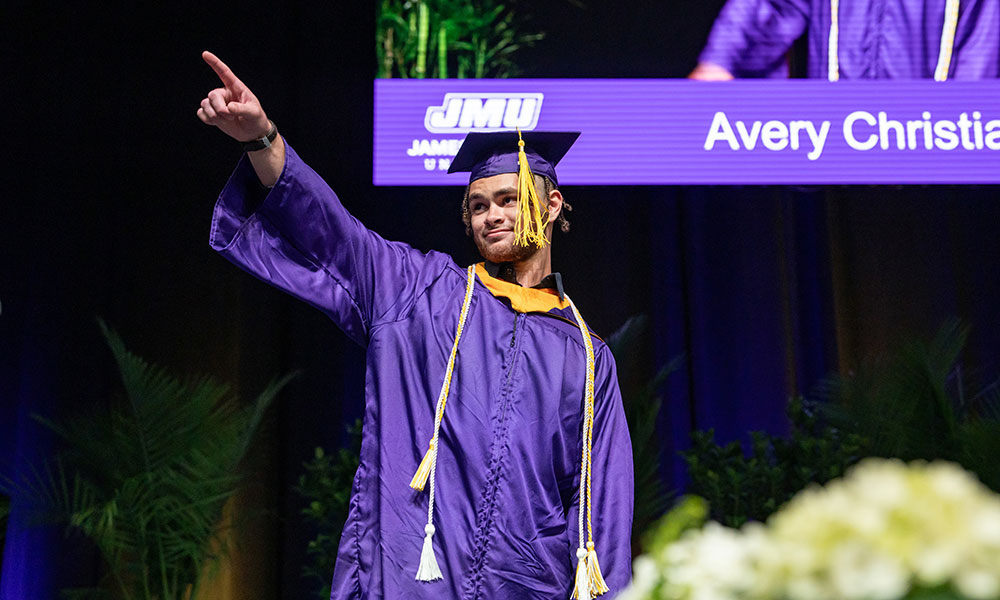Student in grad attire gesturing while standing on stage