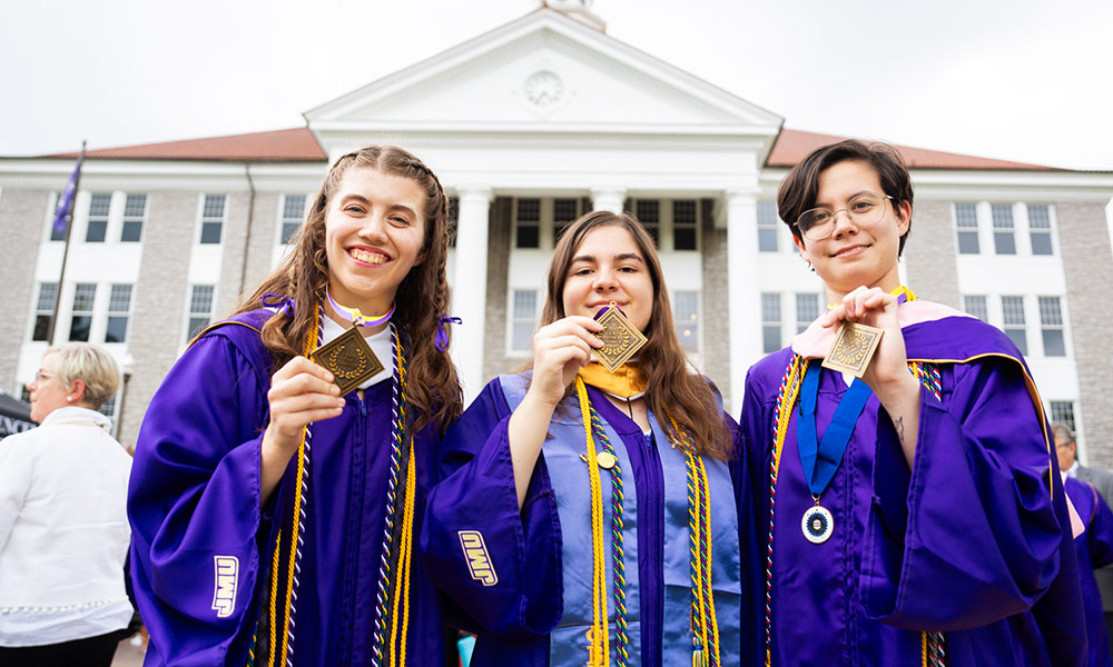 Three students in grad attire showing their honors medallions