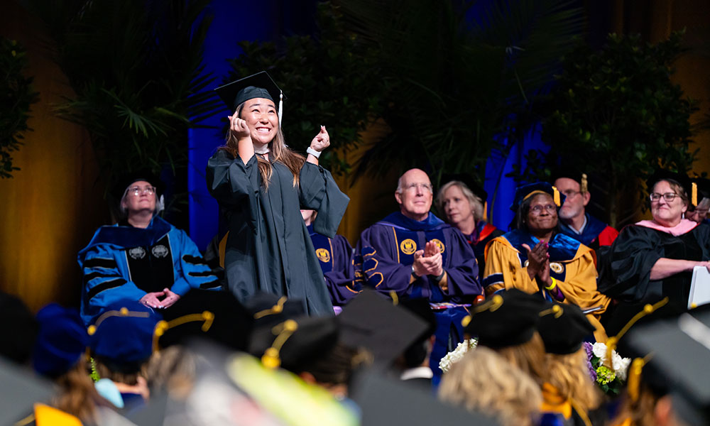 Grad student in graduation attire smiling on stage