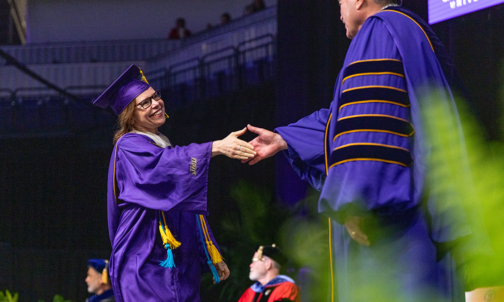 A graduate in a purple cap and gown shakes hands with a dignitary during a graduation ceremony.