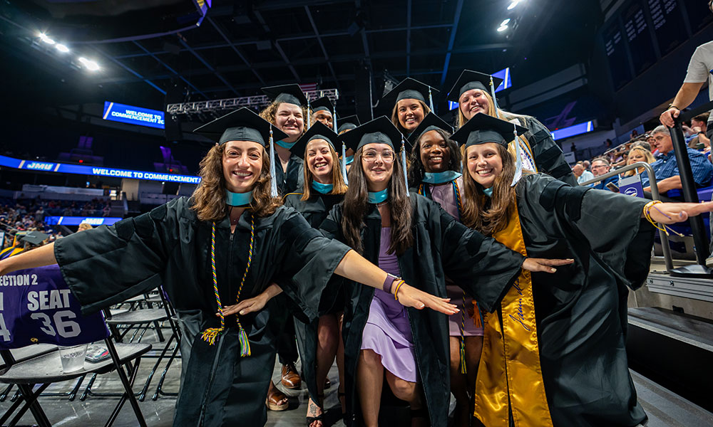 A group of graduates in caps and gowns joyfully celebrating at a commencement ceremony.