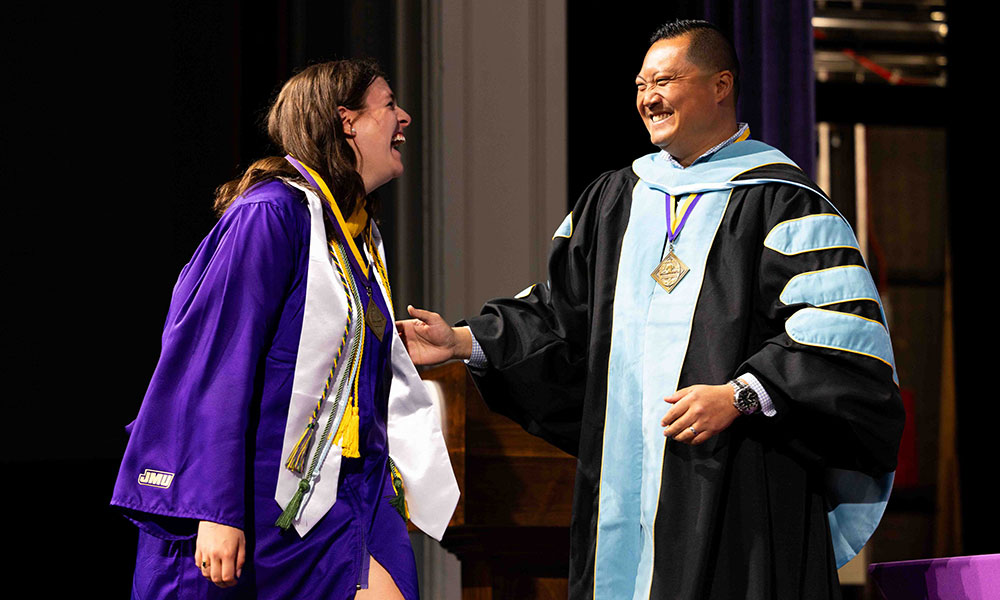 A joyful graduate in a purple robe shares a heartfelt moment with a smiling official in academic regalia during a graduation ceremony.