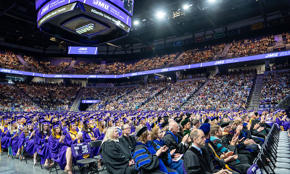 Graduation ceremony at James Madison University, showcasing graduates in purple caps and gowns and a large audience in attendance.