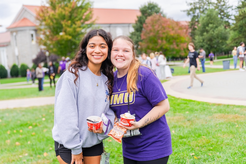 Two students standing on the Quad at JMU smiling and posing together.