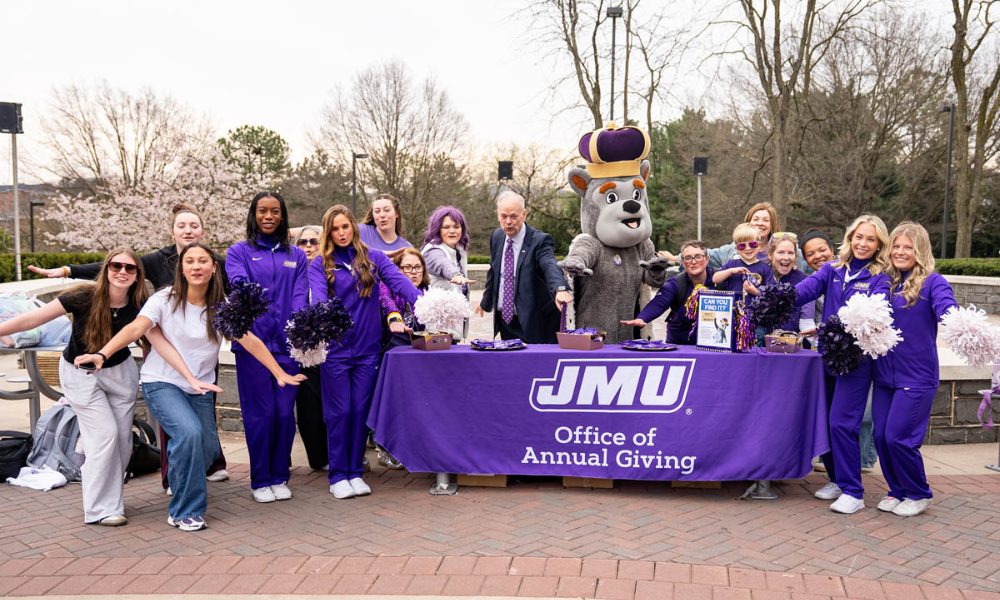 Student, Duke dog and President Schmidt gesturing J-M-U Dukes 
