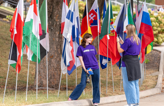 2 students taking a photo with flags of other countries