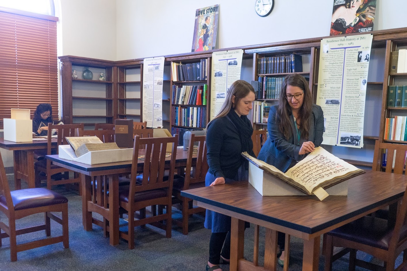 Two women read a large, old book propped up on wedges