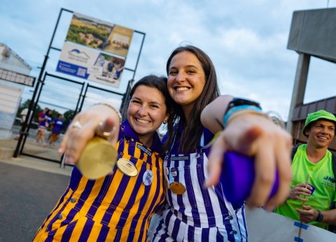 Two students smiling and holding streamers while pointing at the camera.