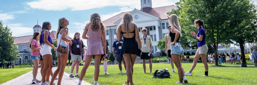 A group of new students standing in a circle participating in an activity on the Quad.