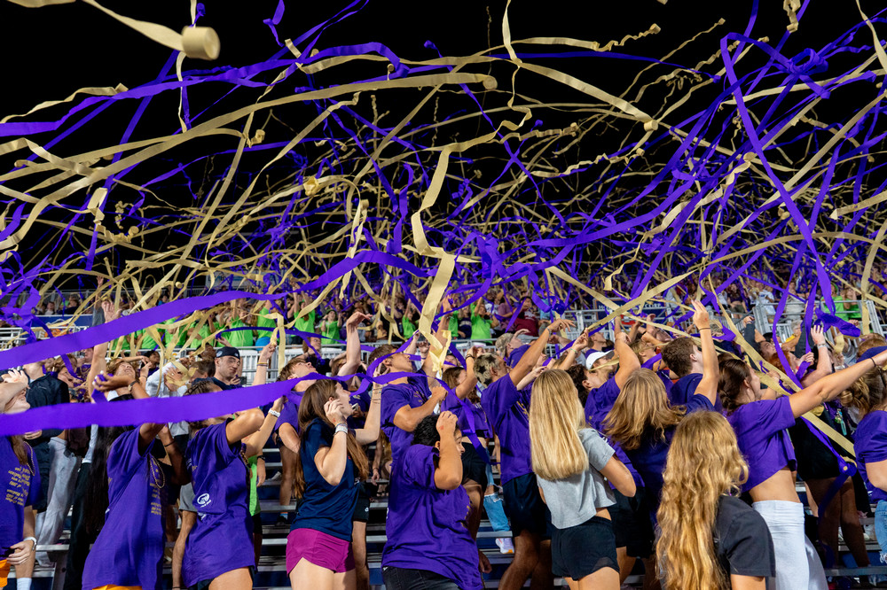 A crowd of students throwing  purple and gold streamers.