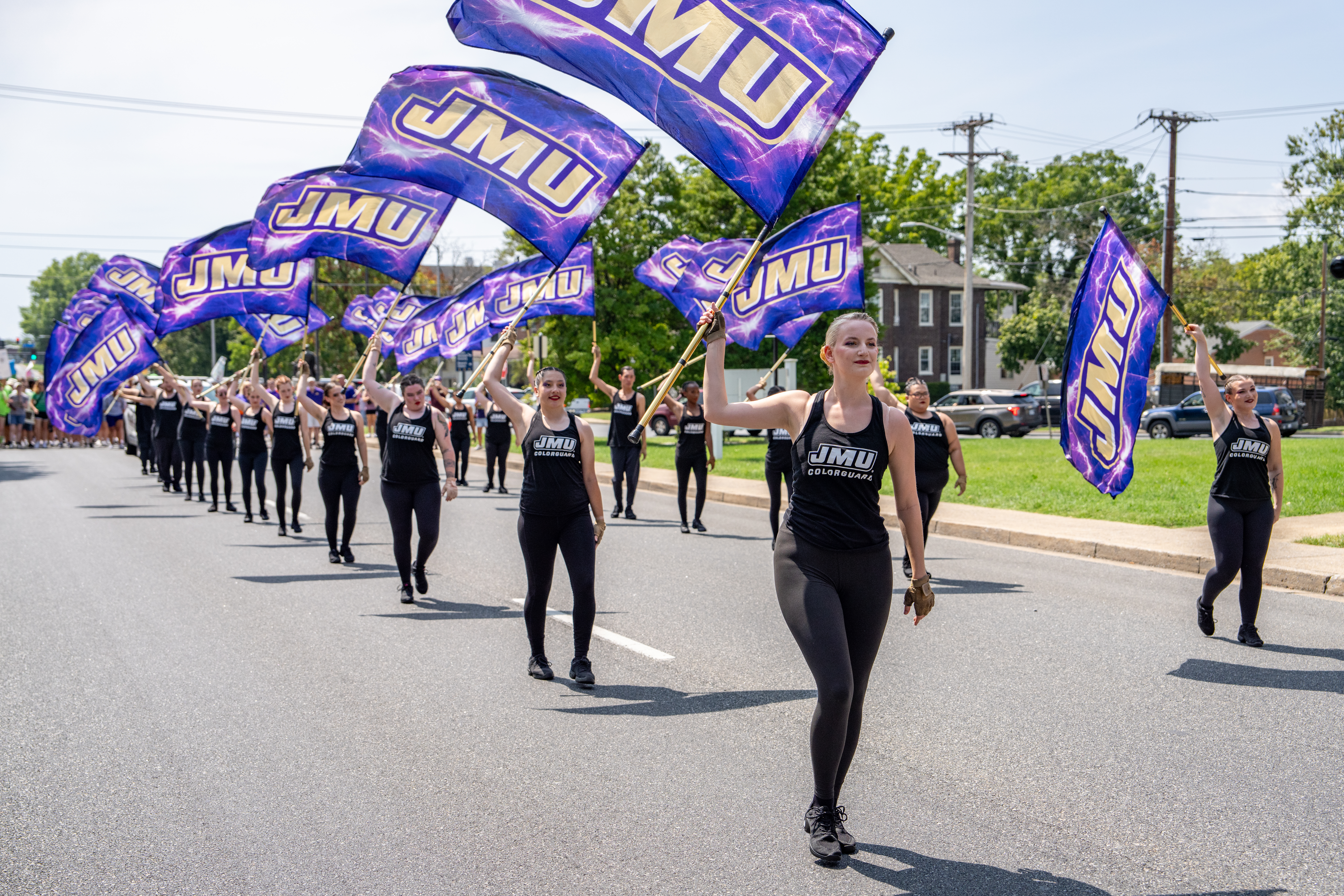 The color guard of the Marching Royals Dukes at JMU marching in a parade with JMU-branded flags.