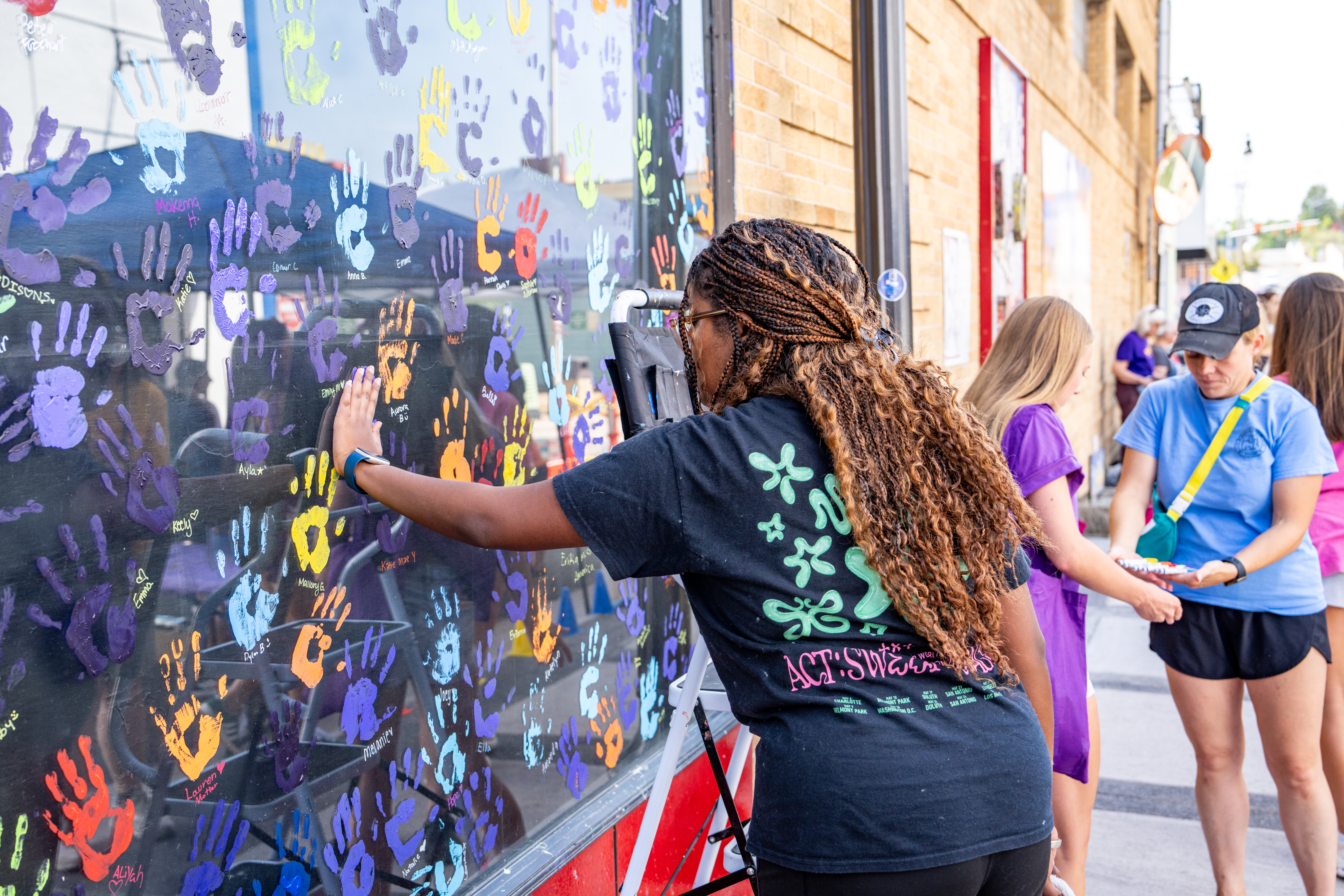 A female student putting her painted handprint on a window in downtown Harrisonburg.