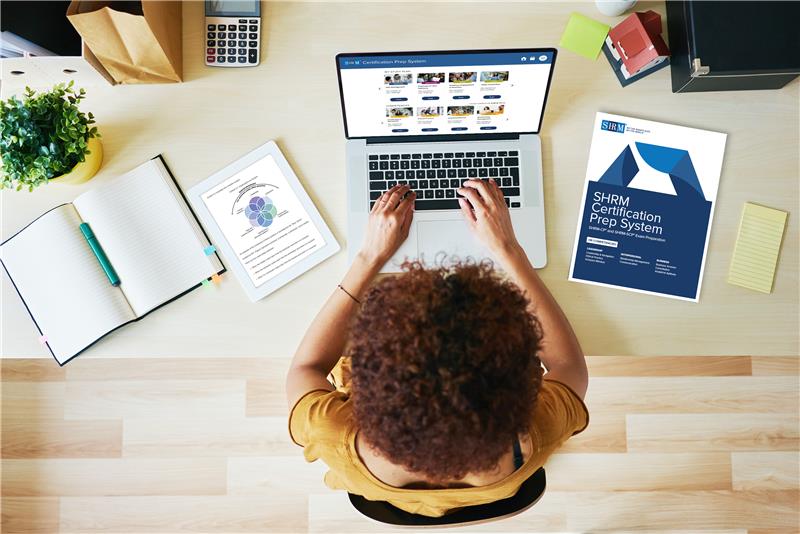 Overhead view of person at laptop with SHRM workbooks 