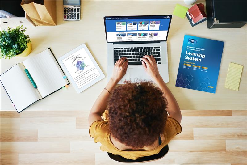 Overhead view of person at laptop with SHRM workbooks 