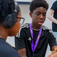 A focused student with a purple lanyard works with classmates on a hands-on project in a classroom setting.
