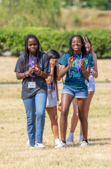 Campers clapping, smiling, and walking in a grassy area on a sunny day