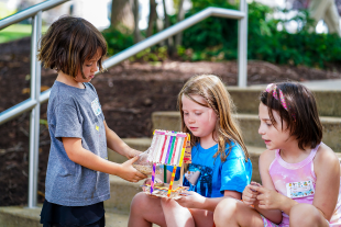 Children engaged in a creative activity, crafting a colorful structure from various materials while seated on outdoor steps.