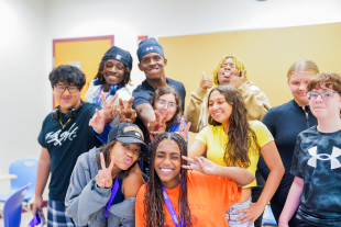 A joyful group of diverse students posing together in a classroom during Science Explorers Camp.