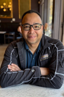 Olympic Fencing instructor smiling at the camera wearing a JMU shirt and black glasses