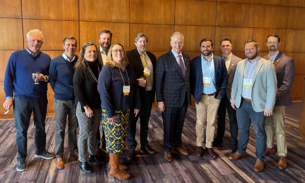 Eleven well-dressed people stand in a loose line for a group photo.