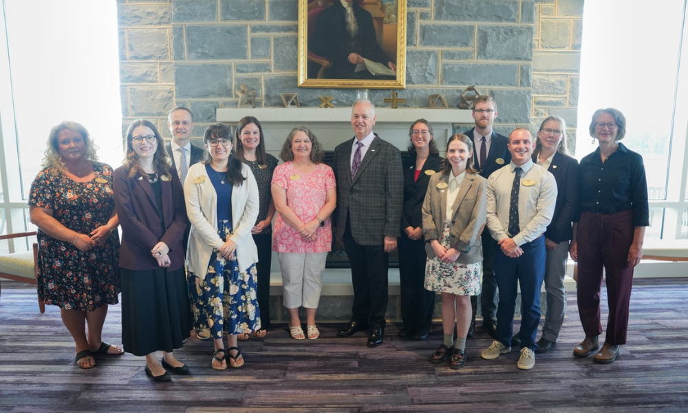 A group of people posing in front of a portrait of James Madison