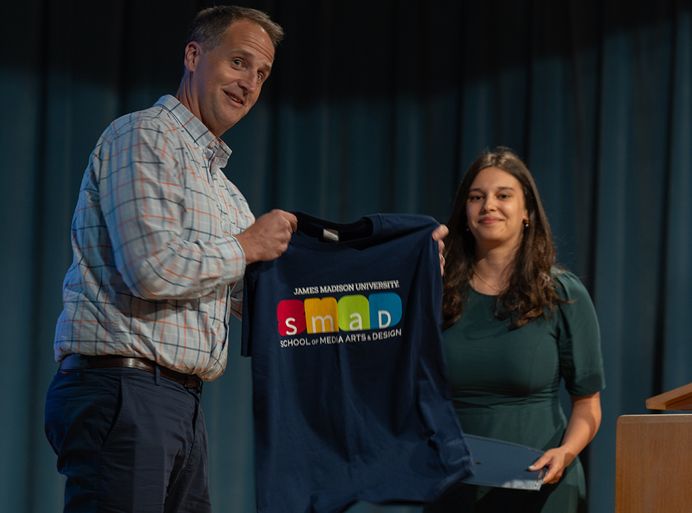 A man holds up a SMAD t-shirt as a woman walks on stage