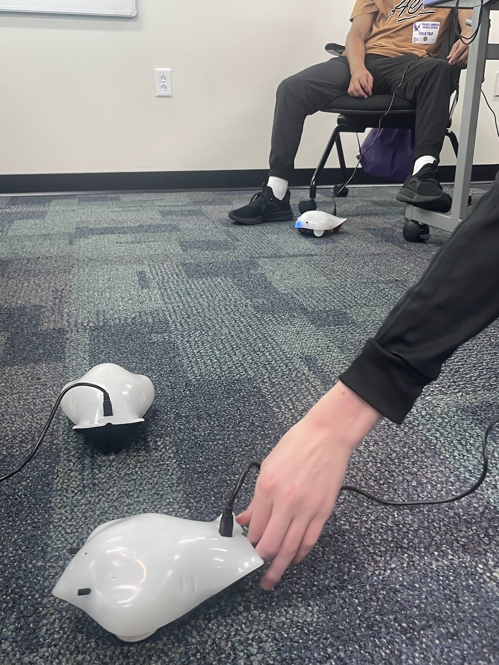 Three finch robots dance on the floor while students watch.