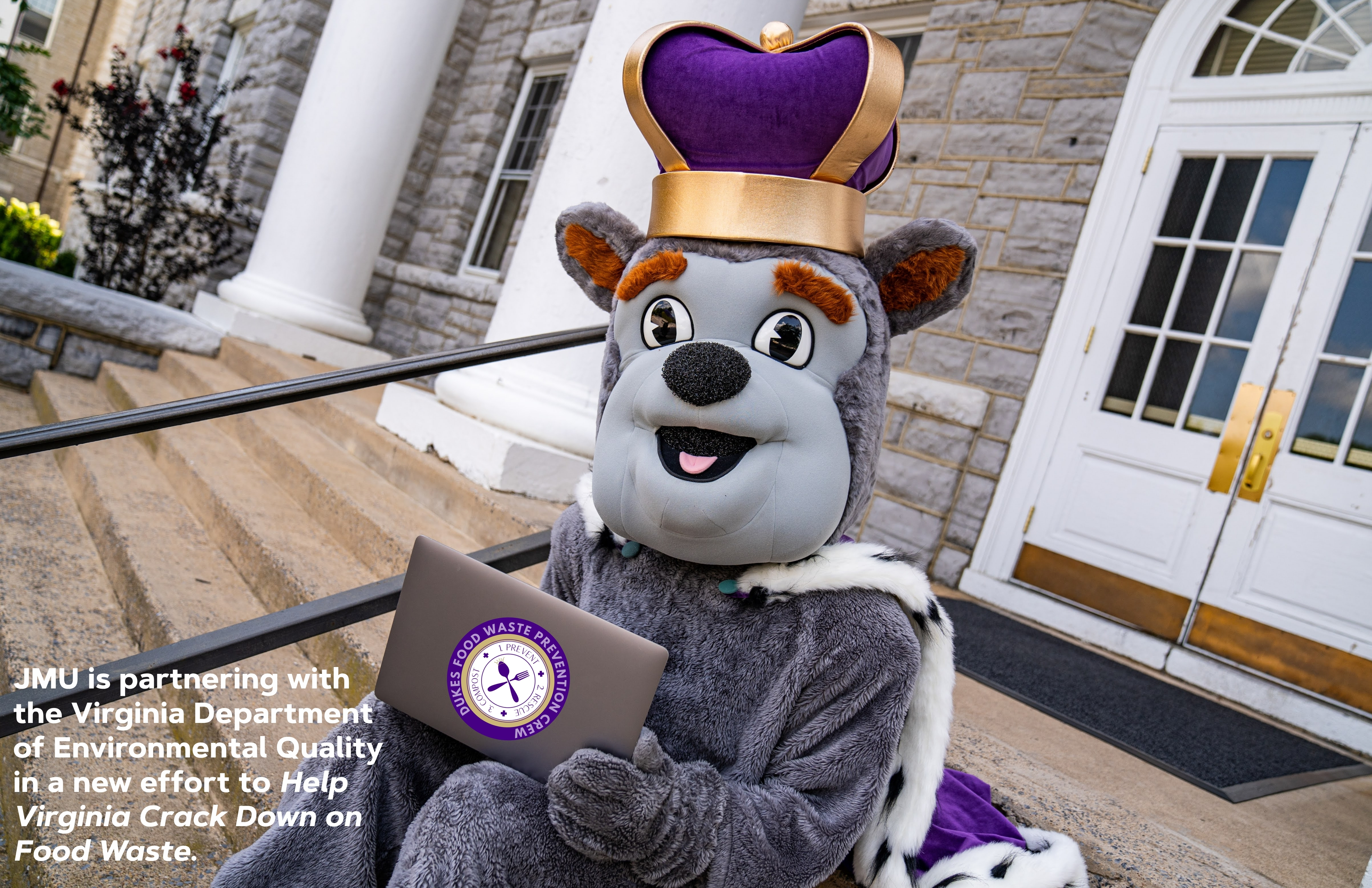 Duke Dog mascot with laptop. Laptop shows a sticker for the Dukes food waste prevention crew.