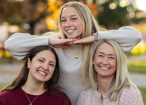 margaret and paige sit on a bench and alli holds her hands under her chin resting on alli and paige's heads